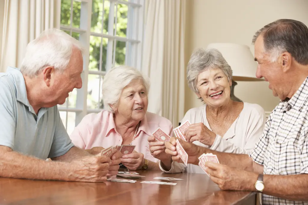 Foto: Vier Seniorinnen und Senioren sitzen gemeinsam an einem Tisch und spielen Karten.