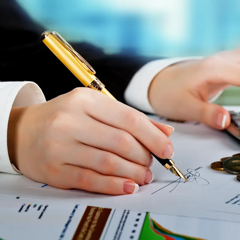 Foto: Symbolbild einer Person, die gleichzeitig etwas in einen Taschenrechner tippt und etwas auf einen Zettel schreibt. Auf dem Papier liegen mehrere Geldmünzen.