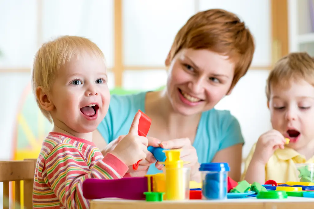 Foto: Zwei spielende Kinder mit einer weiblichen Pflegeperson.