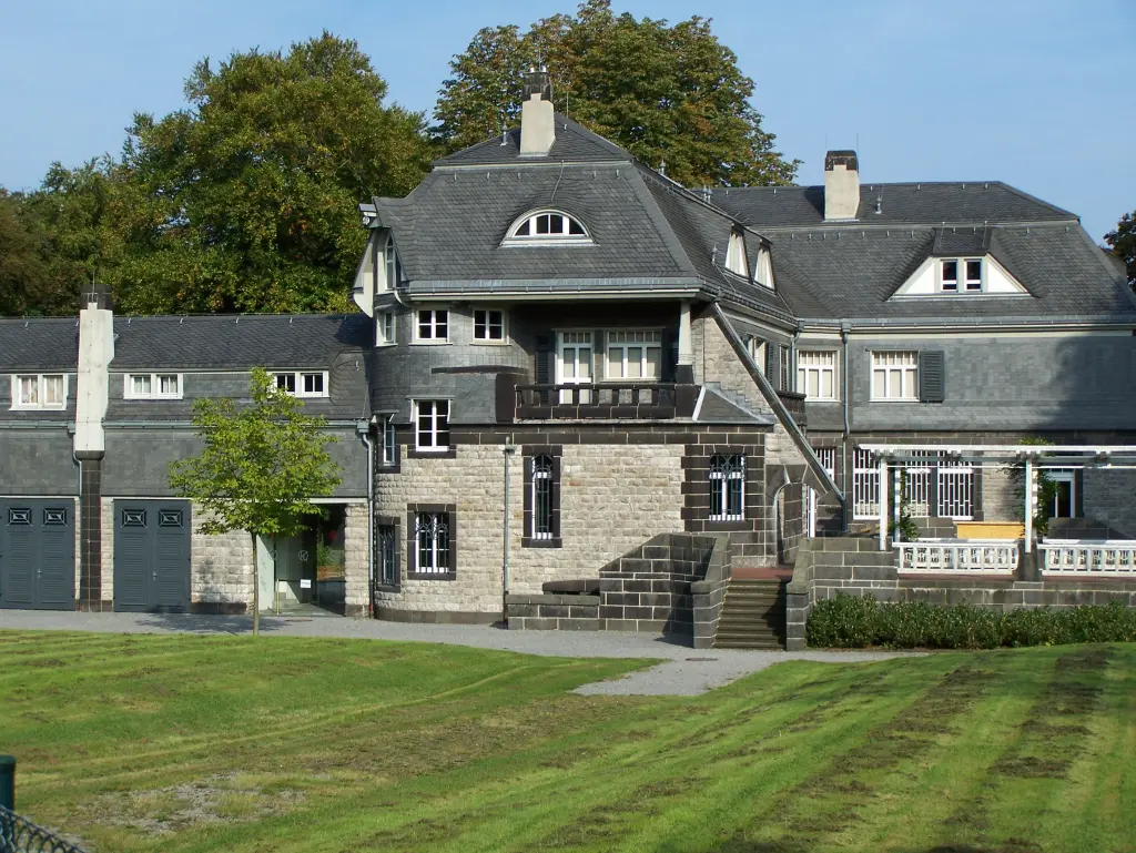 Foto: Eine große schöne Villa mit dunklem Dach, im Vordergrund ein gut gepflegter Rasen.