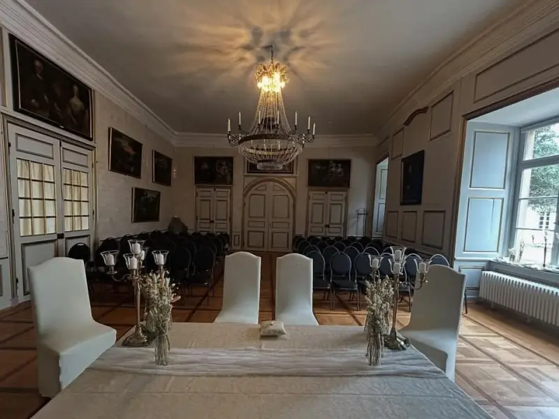 Foto: Ein breiter Tisch mit samtener Tischdecke und mehreren Stühlen in einem Festsaal.