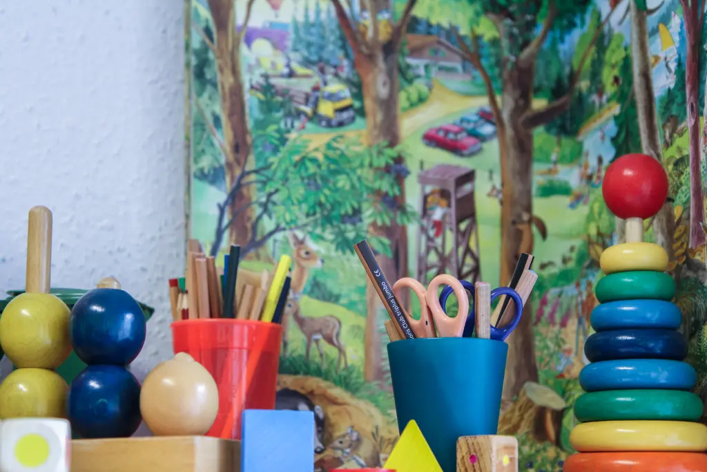 Foto: Eine Spielecke mit Bastelunterlagen, einer Schere und Spielzeugen aus Holz für Kleinkinder.
