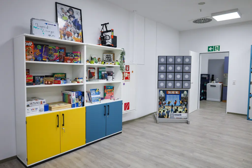 Foto: Die Jugend Lounge Mitte mit einem Schrank voller Brettspiele und Flyer sowie einer Garderobe für Jacken.