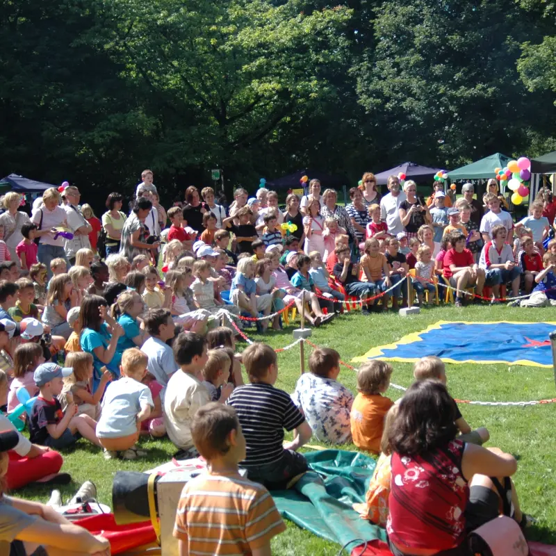 Ein Gruppe von sitzenden und stehenden Kindern und Erwachsenen, die gebannt einem Clown zuschauen.