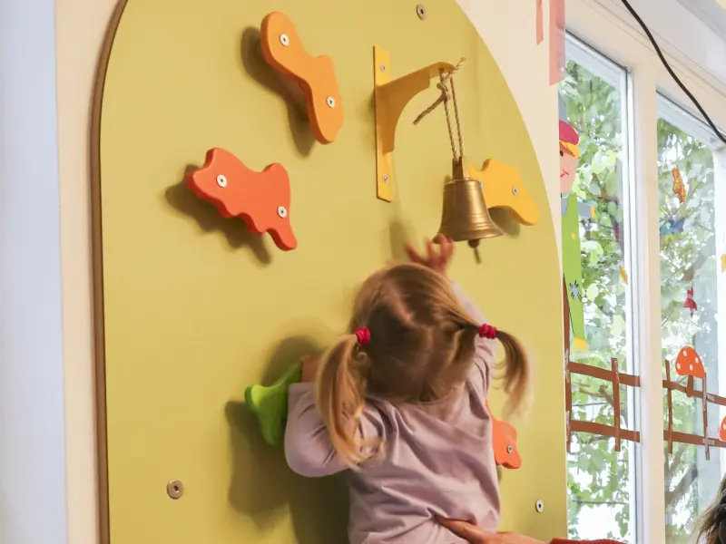 Foto: Ein Kleinkind klettert mit Unterstützung eine altersgerechte Spielwand hoch.