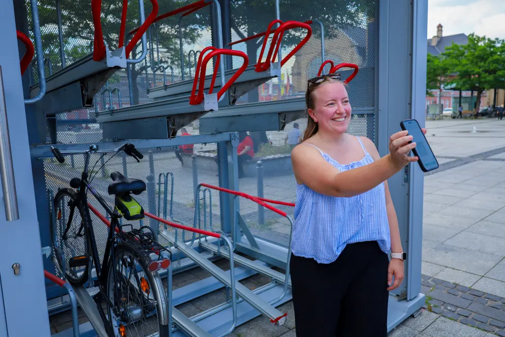 Foto: Eine Frau steht vor der Sammelabstellanlage für Fahrräder am Hagener Hauptbahnhof und hält ihr Handy, mit dem die Anlage geöffnet werden kann, in der Hand.