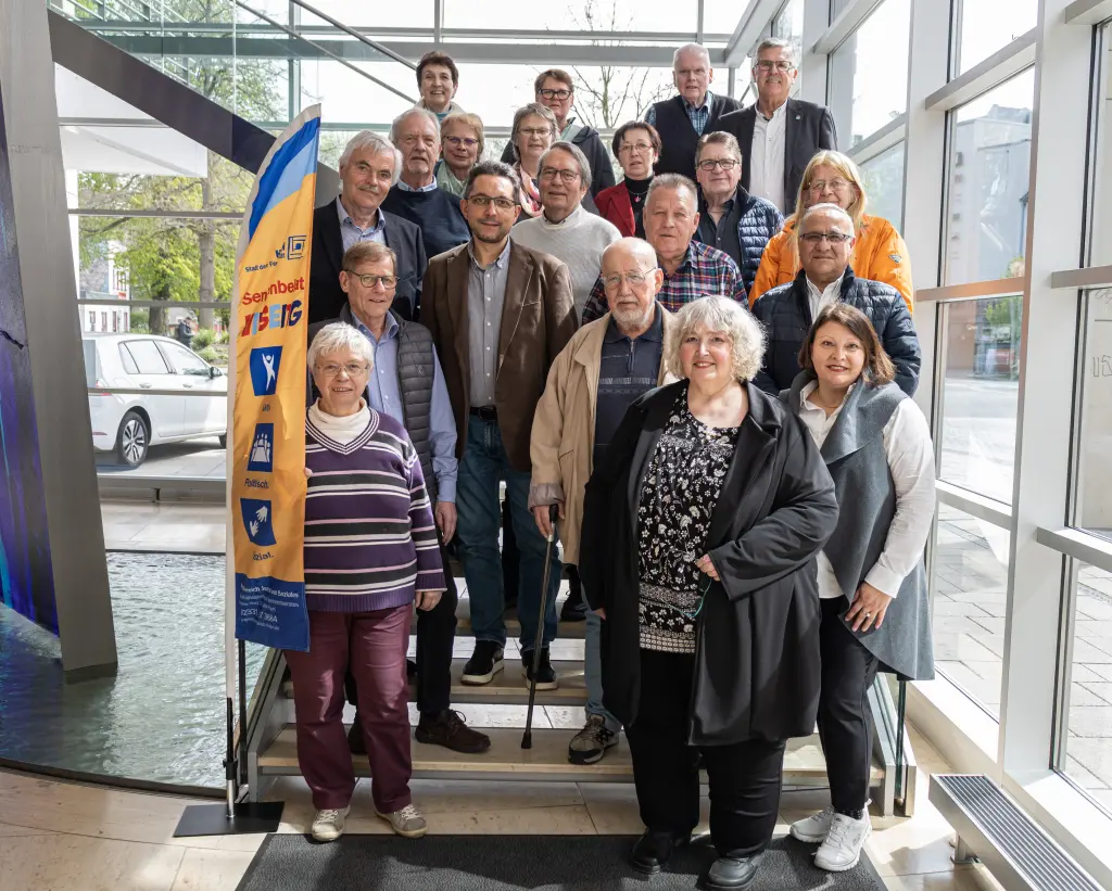 Foto: Der Seniorenbeirat der Stadt Hagen posiert gemeinsam für ein Gruppenfoto auf der Treppe im Rathausfoyer.