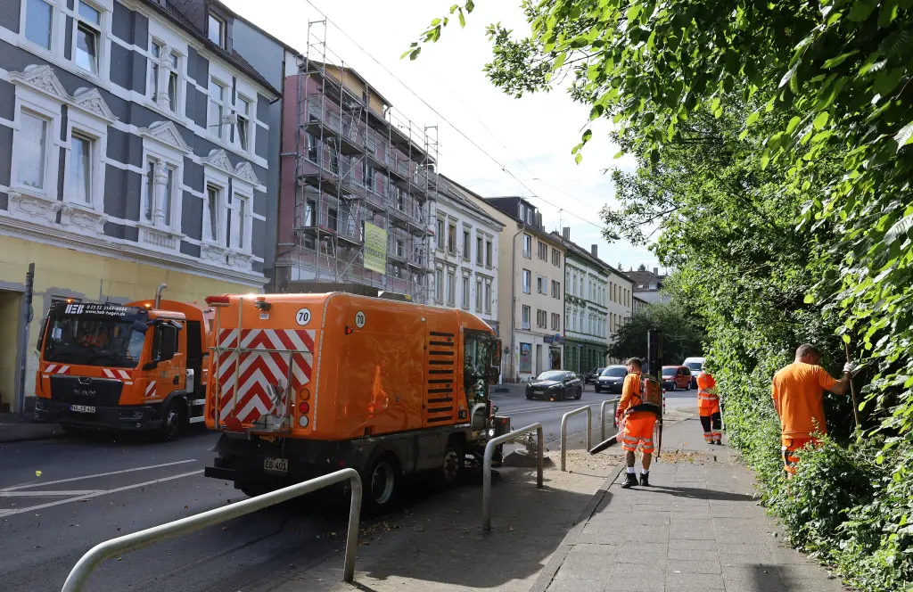 Ein Entsorgungsfahrzeug der Firma HEB steht auf einer Straße, rechts sind Mitarbeitende mit Müllgreifern unterwegs.