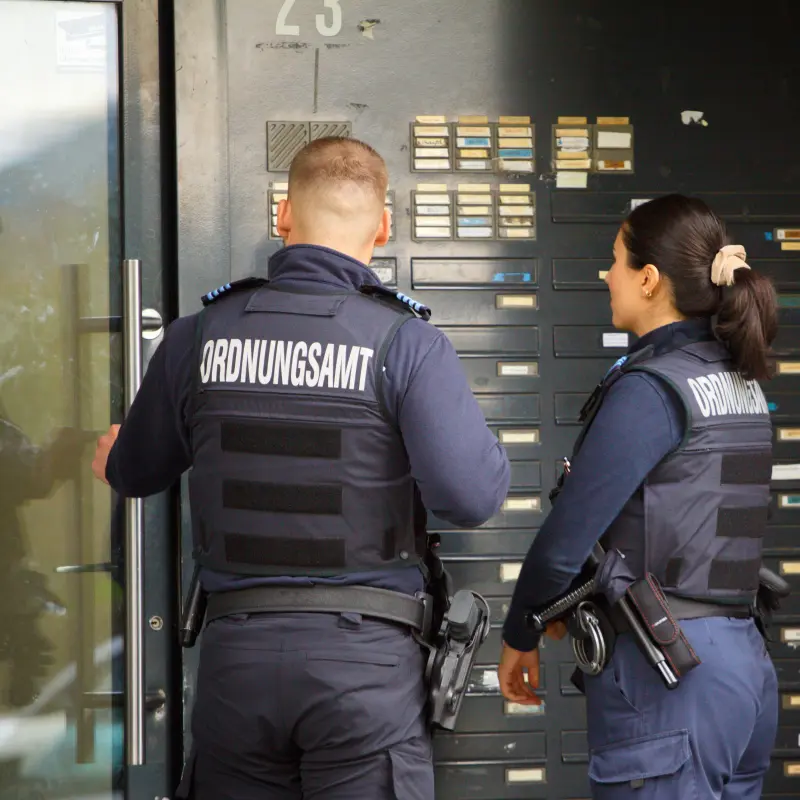 Foto: Zwei Ordnungsbeamte stehen vor einer verschlossenen Haust&uuml;r.