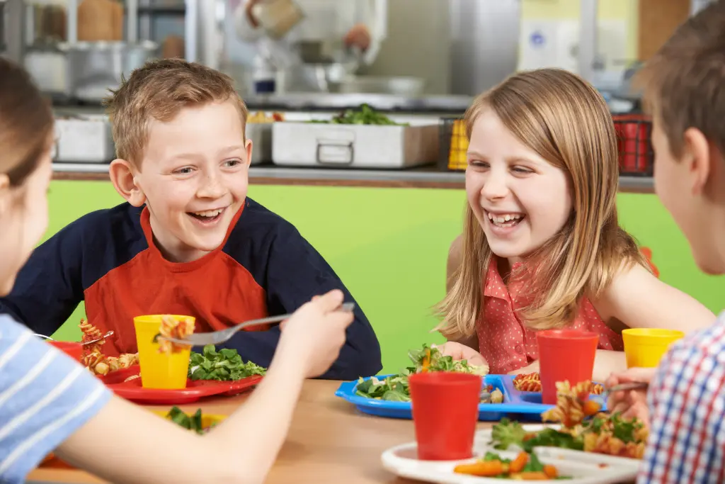 Foto: Drei Kinder sitzen fröhlich am Tisch und essen.