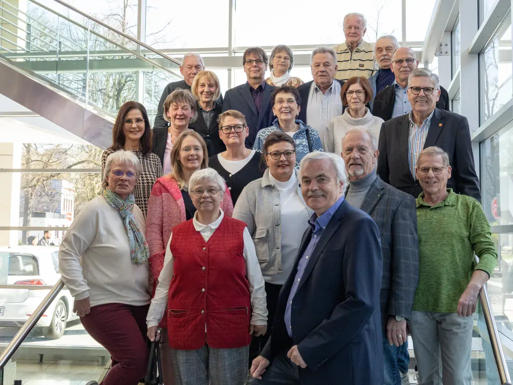 Foto: Der Seniorenbeirat der Stadt Hagen posiert gemeinsam für ein Gruppenfoto auf der Treppe im Rathausfoyer.