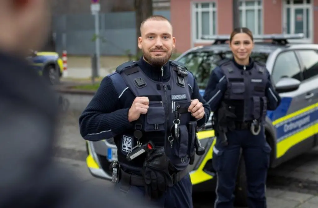 Foto: Ein Mann und eine Frau vom Ordnungsamt stehen vor einem Auto vom Ordnungsamt und schauen in die Kamera.